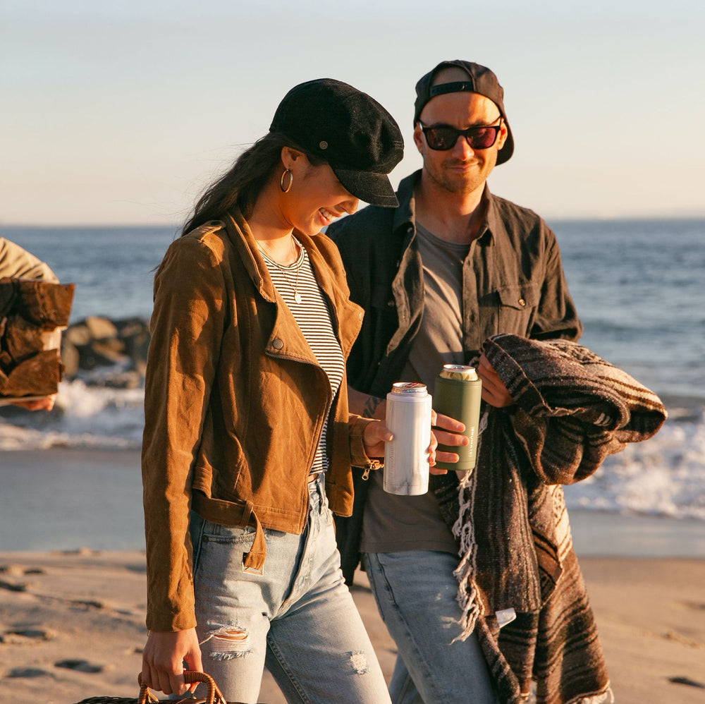 Picture of cool couple walking on the beach in the fall with their Brumate skinny can coolers.